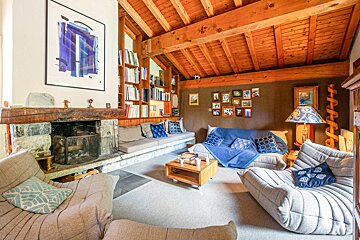 Cozy rustic living room with exposed wood beams, a stone fireplace, Togo-style sofas, and built-in bookshelves.