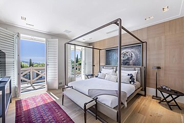 Bright, modern bedroom featuring a four-poster canopy bed, tiger artwork, a wood-paneled wall, and open doors leading to a sunny balcony.