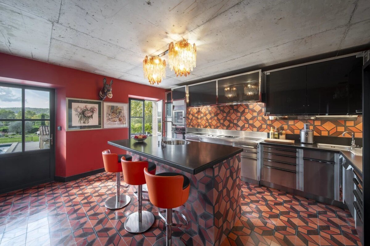 Vibrant modern kitchen featuring red walls, geometric tile floors, black cabinets, and an island with three orange bar stools.
