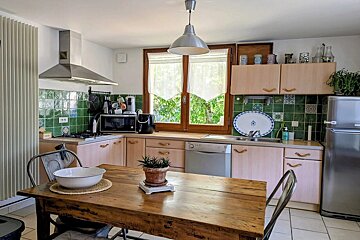 Cozy kitchen featuring green tiled walls, light wood cabinets, and a wooden dining table in the foreground.