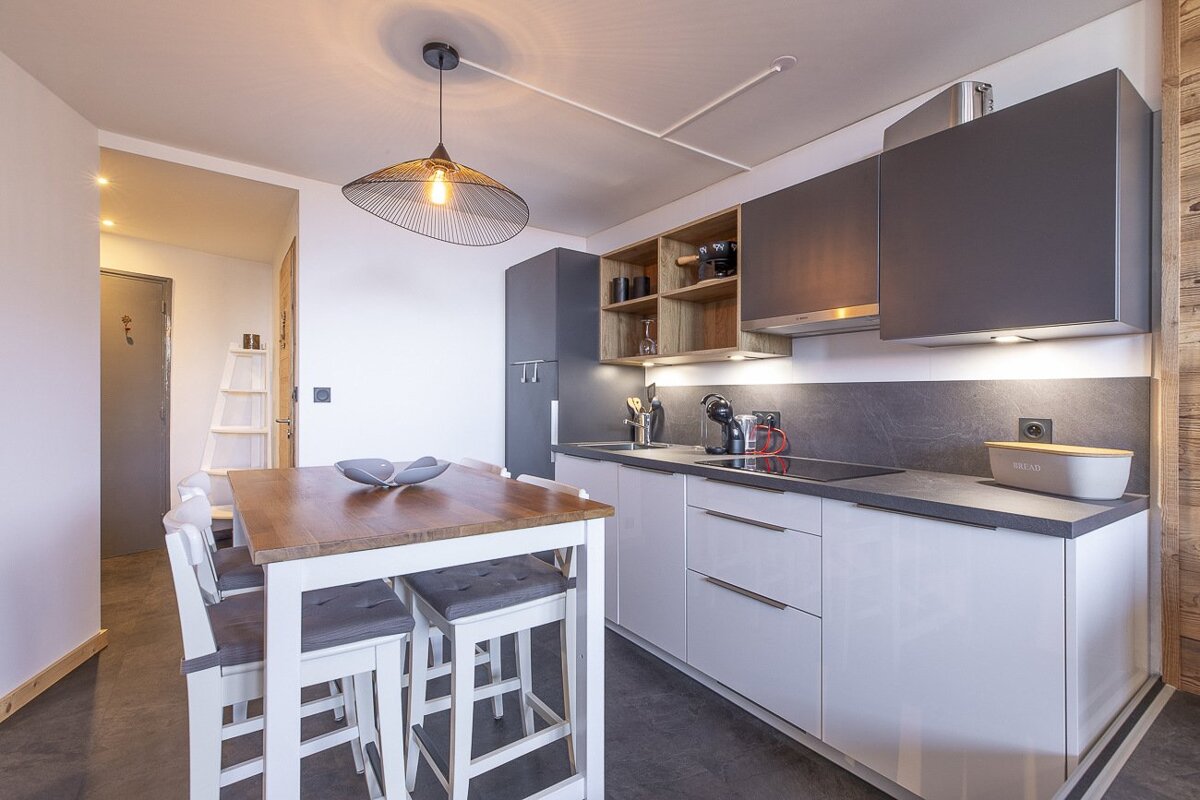 Modern kitchen with white and grey cabinets, a wooden dining table with bar stools, and a pendant light.