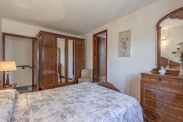 A classic bedroom features a floral-patterned bed, a large wooden wardrobe with mirrored doors, and a dresser with an ornate mirror. Two open doorways are visible.