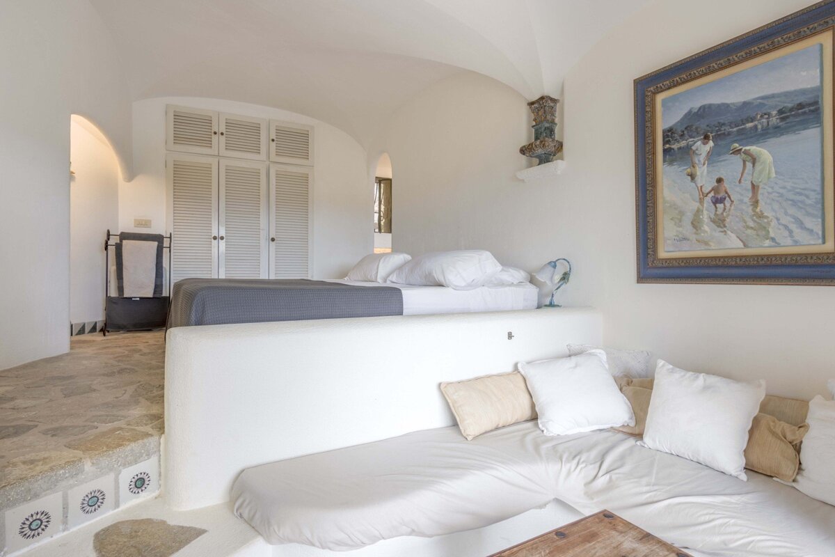 A bedroom with a painting on the wall above the bed