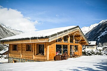 A wooden house with snow on the roof and mountains in the background