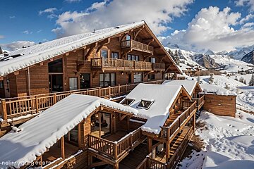 Snow-covered wooden chalets with balconies in a scenic mountain range under a blue, cloudy sky.