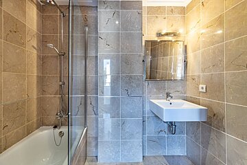 Modern bathroom with shower over tub, wall-mounted sink, mirror, and tiled walls in grey and beige tones.