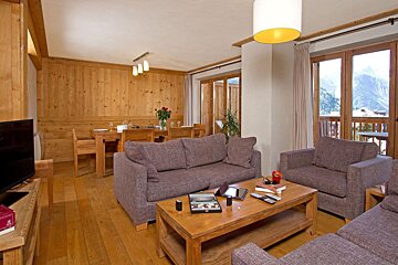 A warm, woody living/dining space featuring comfy sofas, a dining table, and stunning mountain views from large windows.