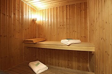 A cozy, empty wooden sauna interior with two benches, a warm wall light, and folded white towels, ready for relaxation.