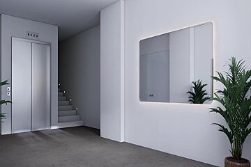 Modern minimalist lobby with an elevator, stairs, a large backlit wall mirror, and a green potted plant.