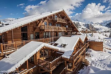 A beautiful, multi-level wooden alpine chalet with snow-covered roofs in a scenic winter mountain landscape.
