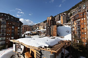 A large ski resort town built on a snowy mountain with many rustic wooden buildings. Blue sky overhead and some construction in the foreground.