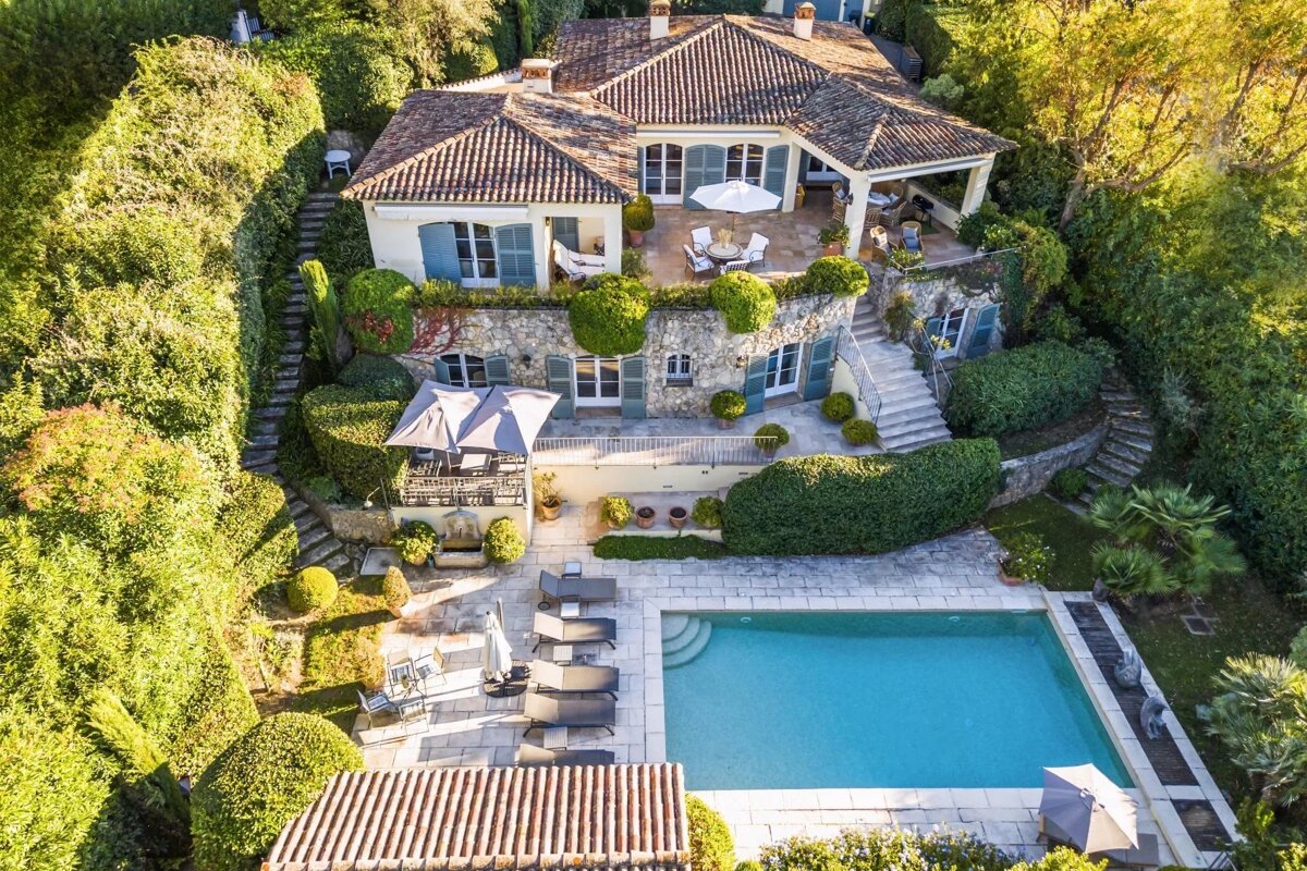 Aerial view of a luxury Mediterranean villa featuring a swimming pool, terraced patios, and lush green gardens.