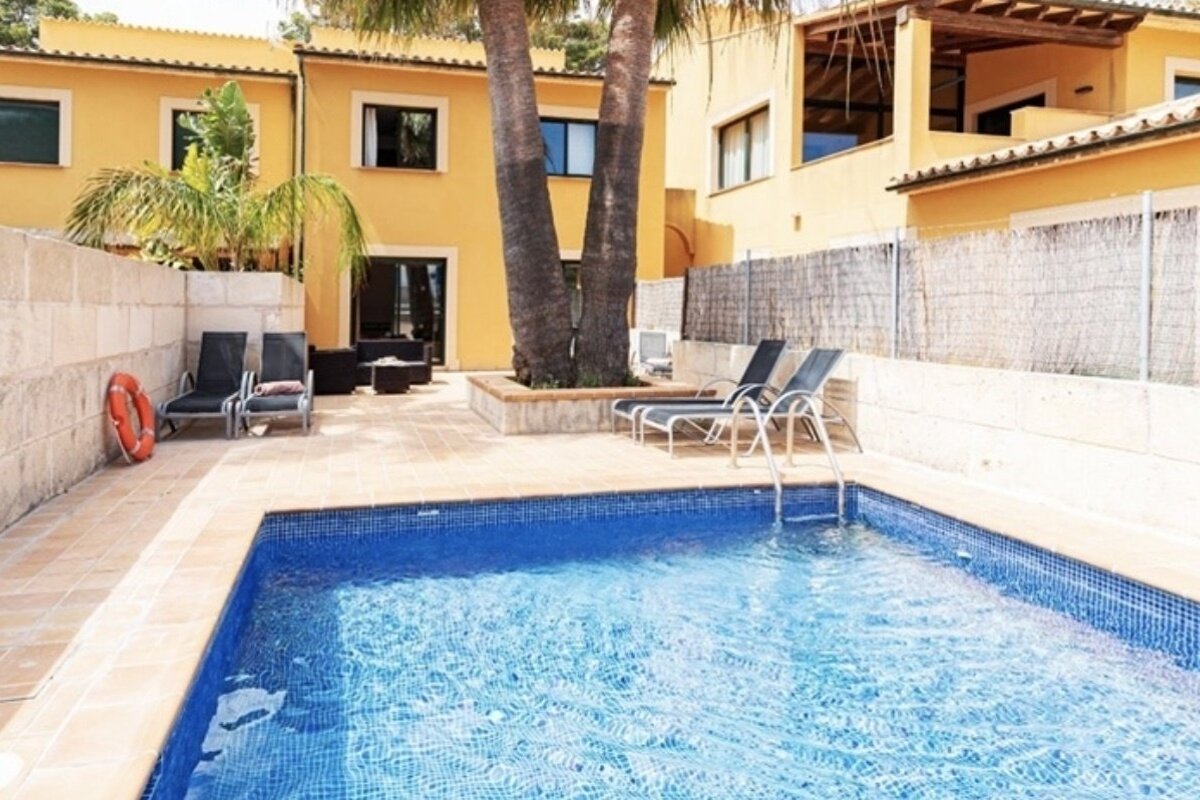 A swimming pool in front of a house with chairs and a life preserver