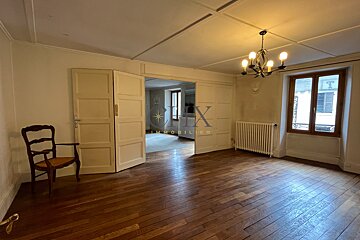 Empty room with wooden floors, a classic wooden chair, open double doors, and a ceiling chandelier lighting the space.