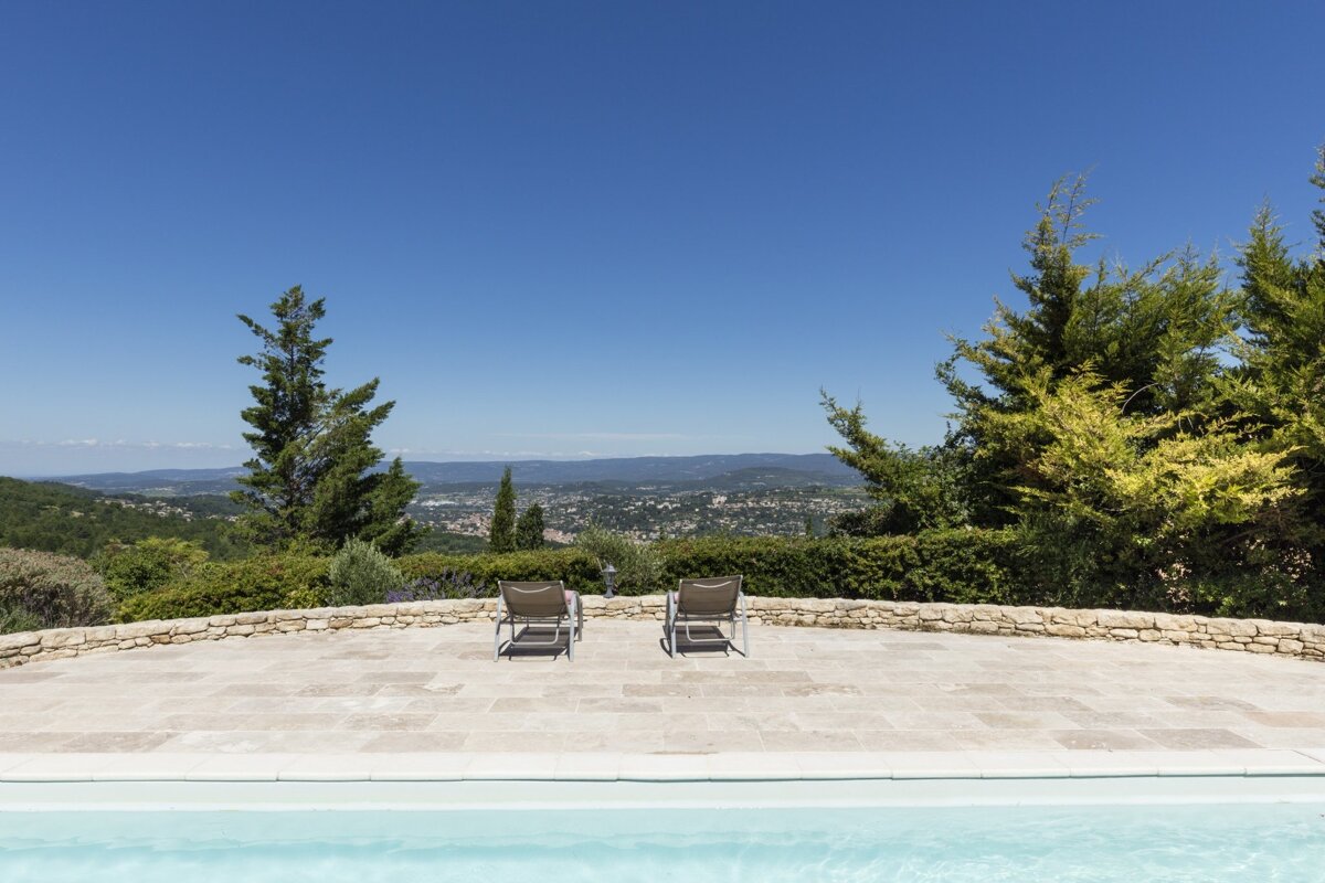 Two chairs sit on the edge of a swimming pool overlooking a city