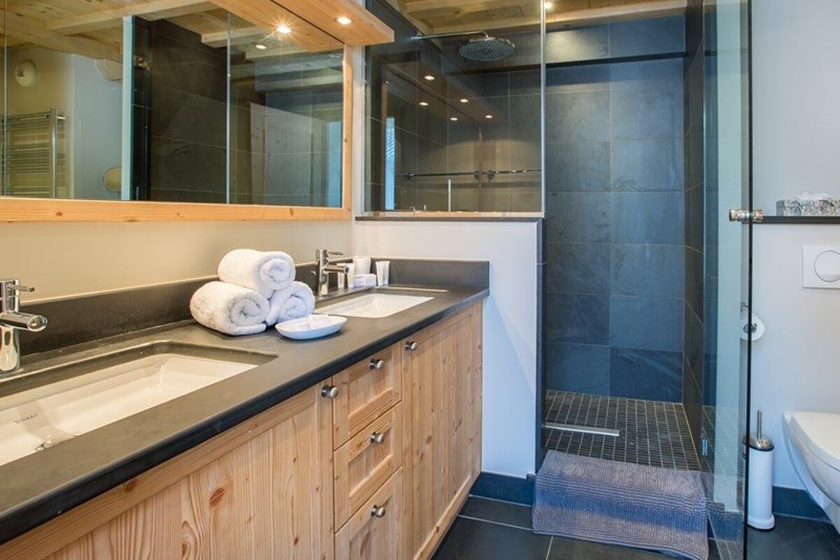 Modern rustic bathroom featuring a wooden double vanity with black countertops and a walk-in glass shower with dark grey slate tiles.