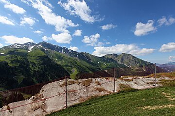 A fence surrounds a grassy hillside with mountains in the background