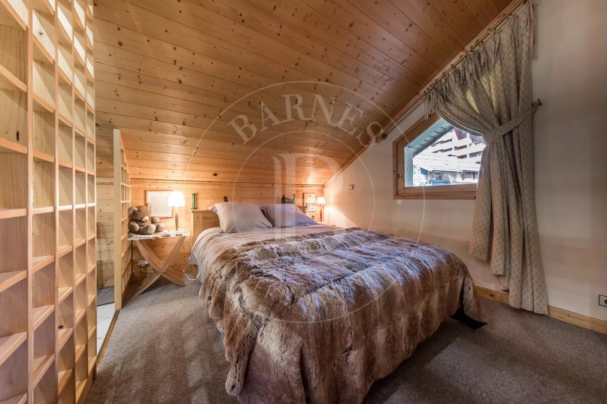 A cozy, wood-paneled attic bedroom features a large bed with a furry blanket, a window with curtains, and built-in shelving, creating a warm ambiance.