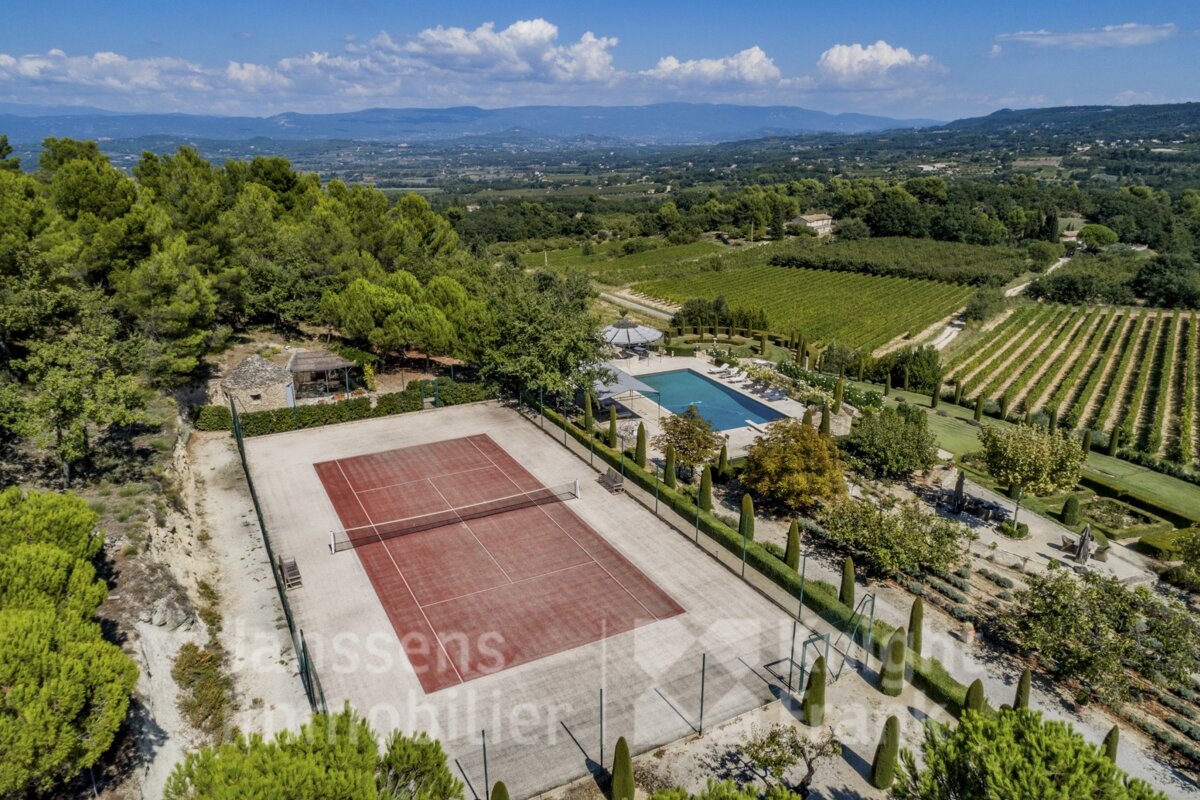 An aerial view of a tennis court surrounded by trees and a swimming pool