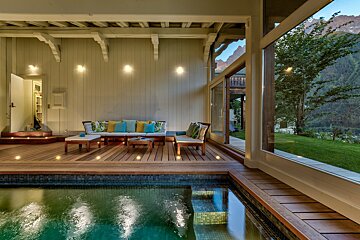 Luxurious indoor pool area with a wooden deck, lounge furniture, and large windows offering a scenic mountain view.