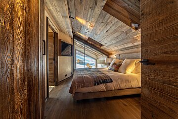 Cozy rustic chalet bedroom with sloped wooden ceilings, a comfortable bed, and a window looking out.