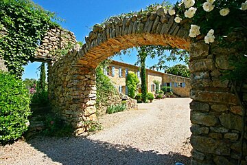 A stone archway leads to a house with blue shutters