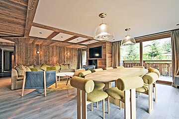 A cozy wooden chalet interior featuring a dining table with yellow chairs and a living room opening to an outdoor balcony.