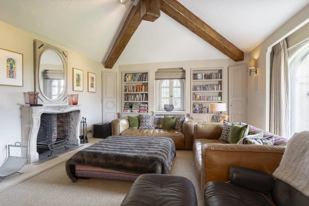 Cozy living room featuring vaulted ceilings with exposed wood beams, brown leather sofas, a large stone fireplace, and built-in bookshelves.
