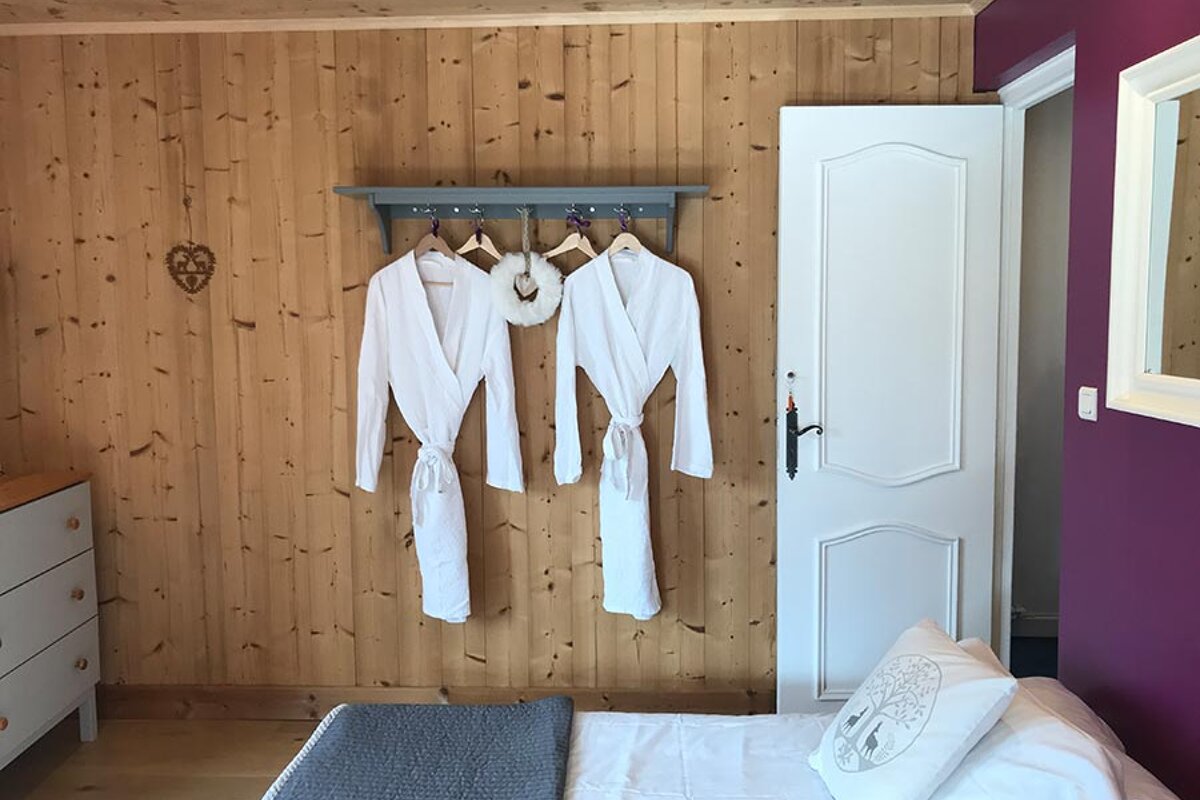 Two white robes hanging on a wooden wall next to a bed