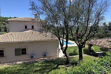 A white house with a tiled roof sits next to a swimming pool
