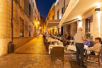 People sitting at tables outside a restaurant with a sign that says ' puerto ' on it