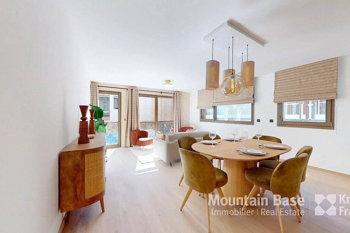 Bright, open-plan living/dining room with modern decor. Features light wood floors, olive chairs, contemporary lighting, and patio views.