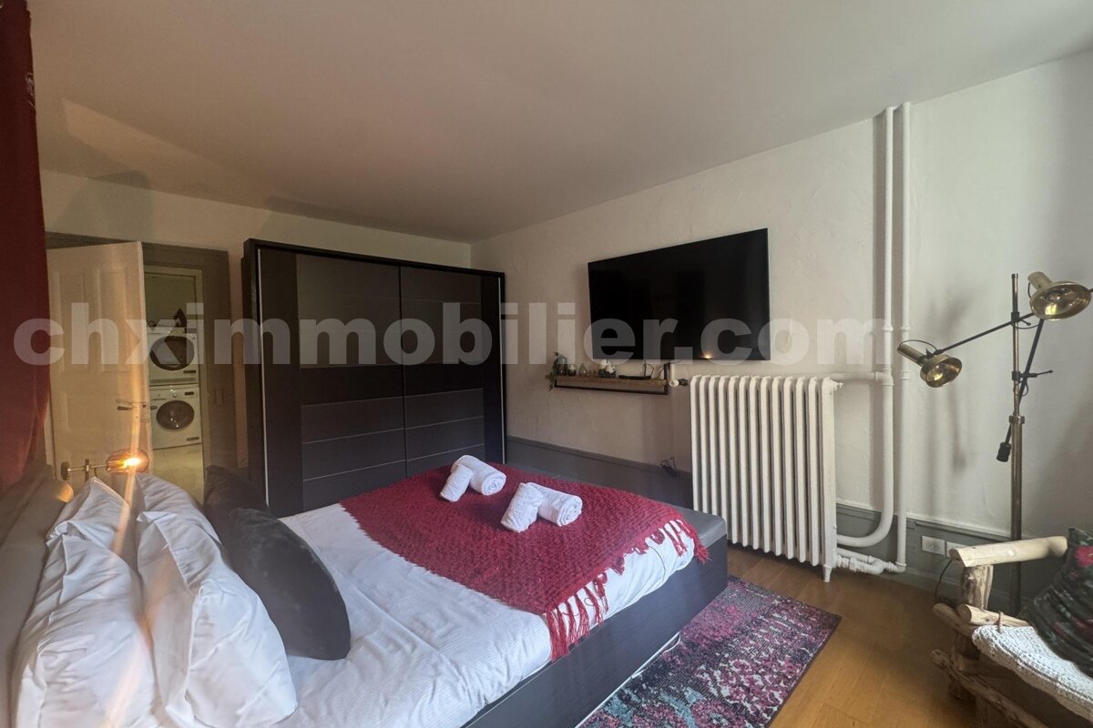 Cozy bedroom with a bed, red blanket, wall-mounted TV, wardrobe, and a glimpse of a laundry room through an open door.
