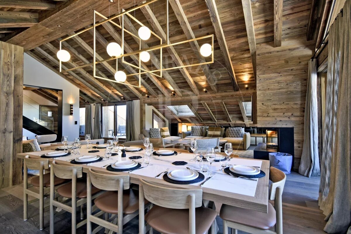 Rustic-chic chalet interior featuring a long set dining table under a modern geometric chandelier and exposed wood beam ceilings.