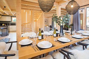 A cozy modern dining room with a set wooden table, sheepskin-draped chairs, and woven pendant lights in a light wood cabin.