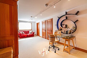 Bright home office featuring a glass desk with a spiral wall bookshelf, wicker chair, and a red sofa in the background.