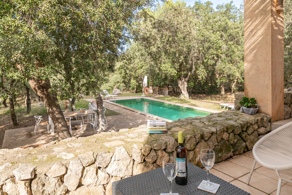 A bottle of wine sits on a table in front of a swimming pool