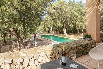 A bottle of wine sits on a table in front of a swimming pool