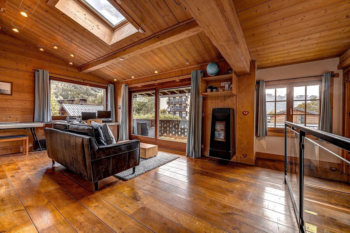 A cozy, wood-paneled room with large windows showing mountain views, a skylight, sofa, and heater, evoking a warm chalet atmosphere.