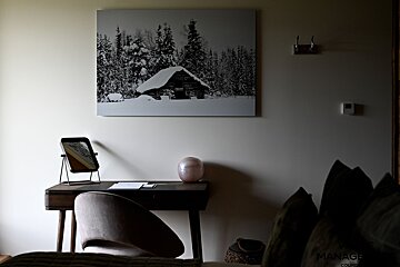 A cozy workspace with a wooden desk and chair beneath a black-and-white canvas print of a snow-covered cabin.