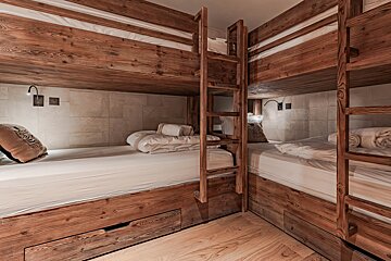Cozy room with rustic, L-shaped wooden bunk beds featuring white bedding, built-in ladders, and under-bed storage drawers.