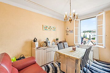 Cozy dining and living space with yellow walls, a red leather sofa, a dining table, and an open window showing city views.