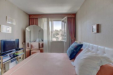 A cozy bedroom featuring a pink bed with a white headboard, a large triptych mirror, and an open window with pink curtains.