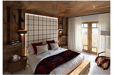 Cozy wooden chalet bedroom with plaid headboard, bed with red accents, and a balcony door revealing a snowy landscape outside.