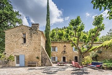 A stone building with blue shutters and a tree in front of it