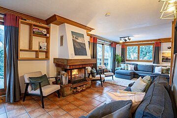 A cozy chalet living room featuring a warm fireplace, comfortable sofas, armchairs, and terracotta tiled flooring.