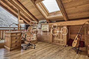 Cozy rustic wooden attic office with a desk, patterned chair, acoustic guitar on a stand, and a skylight.
