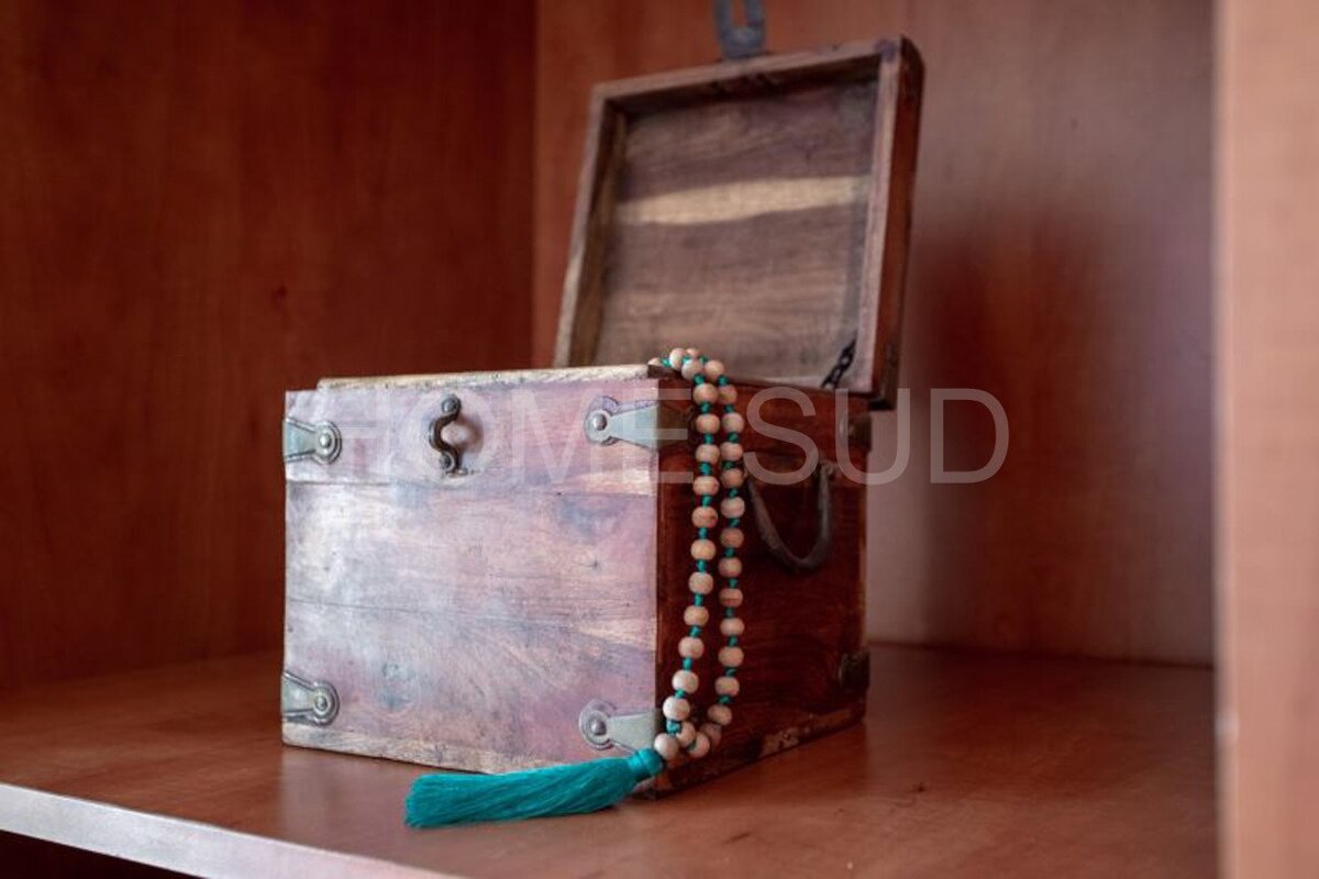 A wooden box with a green tassel sits on a wooden shelf with the word homesud written on the bottom