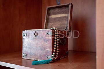 A wooden box with a green tassel sits on a wooden shelf with the word homesud written on the bottom