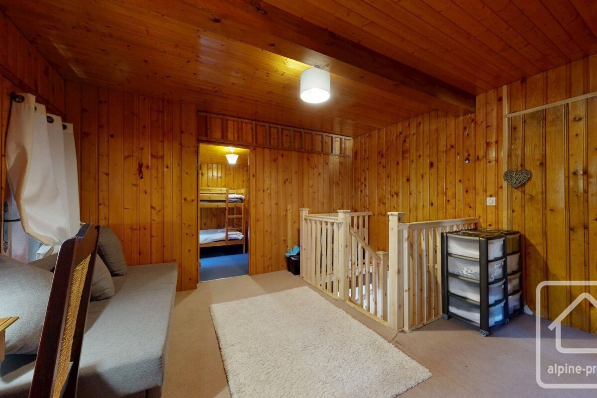 Wood-paneled room with bunk beds visible through a doorway, wooden stairs, a sofa, fluffy rug, and a storage unit.